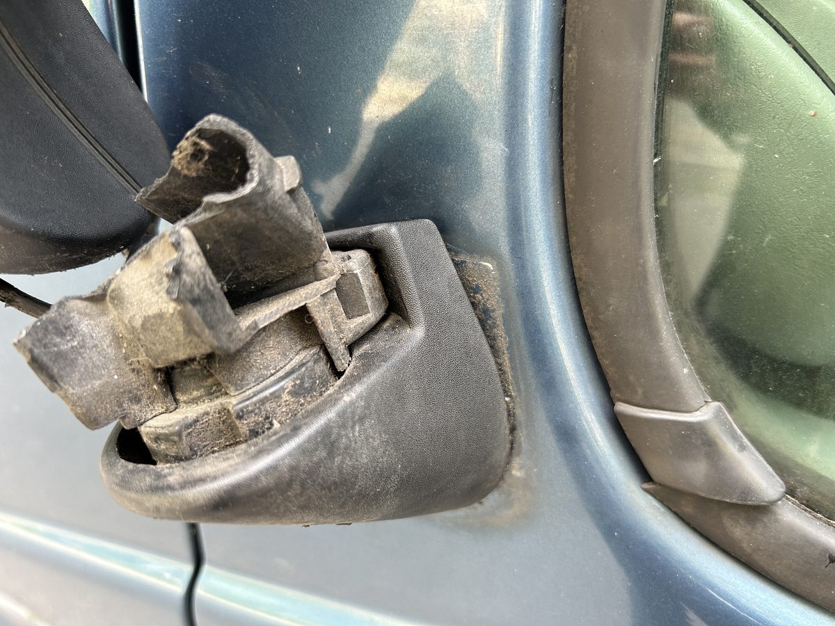 Abgerissener Spiegelfuß am linken Außenspiegel eines blauen Renault Trafic, Halterung gebrochen und Kabel freiliegend